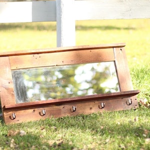 May include: A rustic wooden mirror with a shelf and hooks. The mirror is made from reclaimed wood and has a natural finish. The shelf is perfect for displaying small items, and the hooks are ideal for hanging keys, jewelry, or other accessories.
