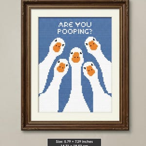 May include: Framed cross-stitch art featuring five white geese with orange beaks and the text "ARE YOU POOPING?" on a blue background. The print is in a brown frame and measures 14.71 x 18.52 cm.