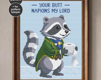 May include: A cross-stitch pattern in a wooden frame featuring a gray raccoon wearing a green coat and blue cravat, holding a roll of toilet paper. The text reads: YOUR BUTT NAPKINS MY LORD. The design measures 7.9 x 10.5 inches and includes a PDF pattern.