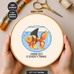 May include: Cross-stitch hoop art featuring a goldfish with a shark fin in a blue bowl. The fish is orange and yellow, with a black fin. The text "MINDSET IS EVERYTHING" is below the fish. The hoop is 5.7 x 6.1 inches.