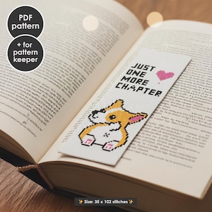 May include: A white bookmark with a pixelated corgi illustration and the text "JUST ONE MORE CHAPTER" with a pink heart. The bookmark is placed in an open book. The size is 35 x 102 stitches.