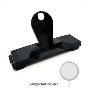 Puede incluir: Un soporte de carga negro impreso en 3D con una base rectangular y un soporte vertical con una abertura circular. El texto "Charger Not Included" es visible. Se muestra un cargador inalámbrico blanco.