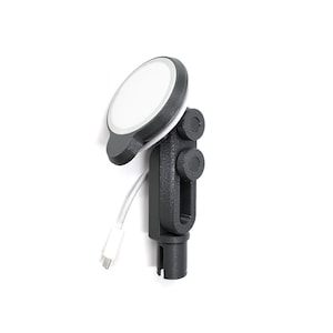 May include: A black and gray phone charger mount with a white charging surface. The mount has a cylindrical base and adjustable knobs. A white charging cable is connected to the charger.