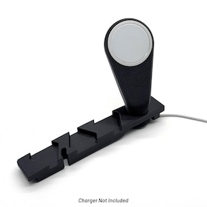 Puede incluir: Soporte de carga negro con una plataforma de carga circular plateada. El soporte tiene un diseño geométrico único con un patrón en zigzag a lo largo de la base. El texto "Charger Not Included" está en la parte inferior.