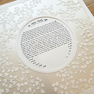 May include: A white and beige wedding ketubah with a circular design featuring a floral pattern and Hebrew text. The text includes the date "October, 2022" and the names "Kevin Daly" and "Hannah Siva Levy".