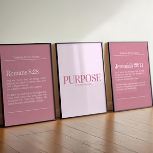 Puede incluir: Tres impresiones artísticas enmarcadas con marcos negros. Las impresiones presentan texto sobre un fondo rosa. Una impresión dice "Romans 8:28", otra dice "PURPOSE" y la tercera dice "Jeremiah 29:11". Las impresiones están apoyadas contra una pared blanca.
