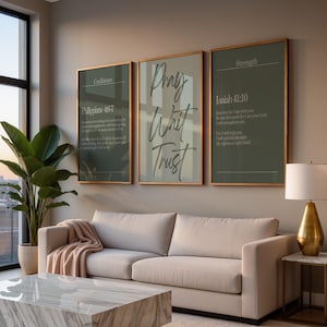 May include: Three framed wall art pieces with gold trim and inspirational text. The center art piece says "Pray, Wait, Trust" in cursive. The other two pieces have Bible verses about confidence and strength. A beige sofa and marble coffee table are in the foreground.