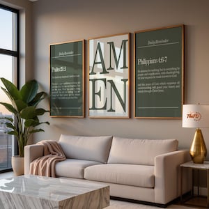 May include: Three framed wall art pieces with gold trim hang above a beige sofa. The art features text, including "AMEN" in large letters, and Bible verses. A marble coffee table and a potted plant are in the foreground.