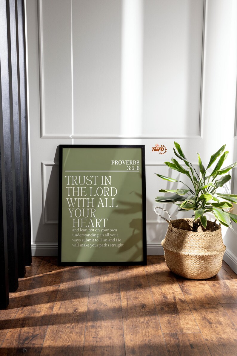 May include: A framed print with the text "TRUST IN THE LORD WITH ALL YOUR HEART" from Proverbs 3:5-6. The print has a green background and is displayed on a wooden floor next to a woven basket with a plant.
