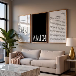 May include: Three framed wall art pieces with gold frames. The art includes the words "BE STILL & KNOW", "AMEN", and a Psalm. The room also features a beige sofa, a marble coffee table, and a potted plant.