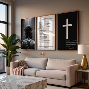 Könnte beinhalten: Drei gerahmte Kunstwerke hängen über einem beigen Sofa. Die Kunstwerke umfassen ein Schwarz-Weiß-Bild einer Person, eine Textseite mit dem Titel "Ein Psalm Davids" und einen schwarzen Hintergrund mit einem weißen Kreuz und Text. Ein Marmor-Couchtisch und eine goldene Lampe sind ebenfalls zu sehen.
