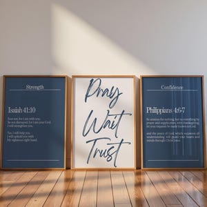 Op de afbeelding: Drie ingelijste wandkunstprints met houten lijsten. De linker print is donkerblauw met witte tekst die Strength en Isaiah 41:10 leest. De middelste print is wit met donkerblauwe scripttekst die Pray Wait Trust leest. De rechter print is donkerblauw met witte tekst die Confidence en Philippians 4:6-7 leest.