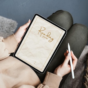 Può includere: Un tablet digitale che mostra un diario di lettura con uno sfondo color beige dalla texture di carta stropicciata. Lo schermo presenta il testo Reading journal in un carattere corsivo marrone, incorniciato da un sottile bordo marrone, tenuto con una penna stilo bianca.