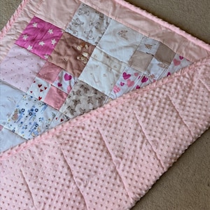 May include: A baby quilt with a patchwork design. The quilt features fabrics with star, heart, and teddy bear patterns in pink, white, and brown. The backing is a soft, textured pink fabric.