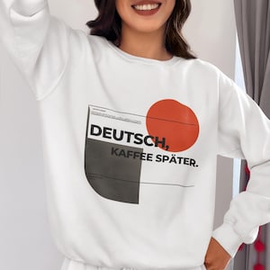 May include: White sweatshirt with the text "DEUTSCH, KAFFEE SPÄTER." in black, with a red circle and a black and gray shape. The Etsy shop name "littlelightorstudio.etsy.com" is also visible. The sweatshirt is part of a matching set.