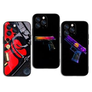 May include: Three black phone cases with gun designs. One case features a red and black design with bullet casings. The second case has a colorful gun graphic. The third case displays a purple and blue gun graphic with a sunset.
