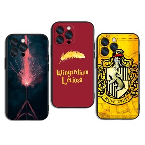 Könnte beinhalten: Drei Handyhüllen mit verschiedenen Designs. Eine Hülle ist schwarz mit einem rosa Knallbonbon-Design. Eine andere ist rot mit einer Feder und dem Text "Wingardium Leviosa". Die dritte ist gelb mit einem Hufflepuff-Wappen.