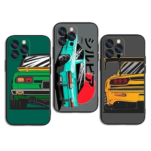 May include: Three phone cases with car designs. One case is green with a yellow stripe and a white car design. The second case is gray with a teal car design and Japanese text. The third case is gray with a yellow car design.