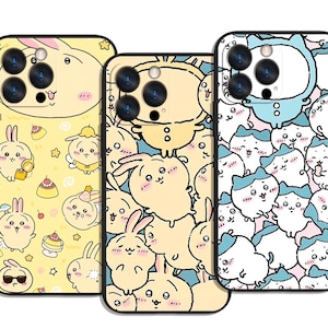以下が含まれることがあります： 黒い縁取りの携帯電話ケース3つ。ケースには、黄色、水色、白のウサギや猫のようなキャラクターの漫画イラストが描かれています。デザインにはデザートと星が含まれています。