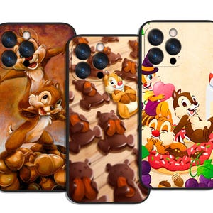 Può includere: Tre custodie per telefono con Cip e Ciop. La prima custodia ha uno sfondo marrone con Cip e Ciop in piedi sulle ghiande. La seconda custodia ha uno sfondo in legno con Cip e Ciop e orsetti di cioccolato. La terza custodia ha uno sfondo color crema con Cip e Ciop e una ciambella.