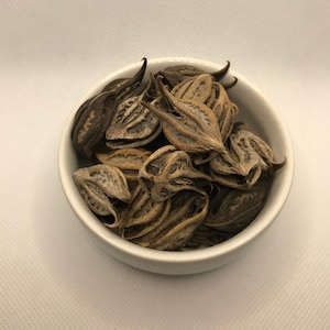 May include: A white bowl filled with dried brown seed pods. The pods are arranged in a random pattern and have a slightly textured surface.