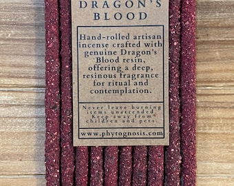 May include: A bundle of dark red, textured incense sticks with a tan paper label featuring the text DRAGON'S BLOOD, a leaf icon, and a description of the hand-rolled artisan incense, including safety warnings and the website www.phytognosis.com.