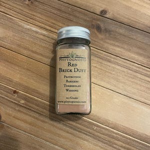 May include: A clear glass jar with a silver screw-top lid containing red brick dust. The label reads Phytognosis Red Brick Dust, Protection, Barriers, Thresholds, Warding, 120 Grams, and www.phytognosis.com. The jar is filled with a fine red powder.