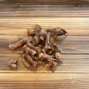 Puede incluir: Un montón de trozos de raíz de galanga seca sobre una superficie de madera. El galanga es de color marrón y tiene una textura rugosa.
