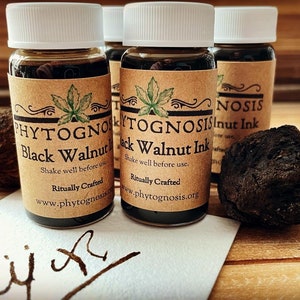 Peut inclure: Trois petits flacons en verre remplis de liquide brun foncé, étiquetés "PHYTOGNOSIS Black Walnut Ink" et "PHYTOGNOSIS Black Walnut Ink". Les flacons sont sur une surface en bois avec une coque de noix noire à côté. Le texte "Ritually Crafted" et "www.phytognosis.org" est imprimé sur les étiquettes.