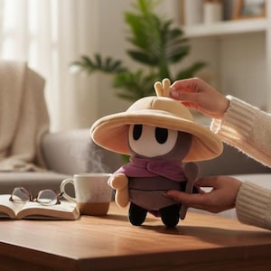 May include: A plush toy character with a wide-brimmed hat, a purple scarf, and a brown body. The toy is on a wooden table with a cup of coffee, an open book, and eyeglasses. The background includes a couch and a plant.