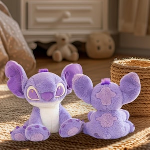 Puede incluir: Dos peluches de Stitch en un tono lila claro, con grandes orejas y ojos expresivos. Uno está sentado, el otro está mirando hacia adelante. Los muñecos están sobre una alfombra tejida, lo que sugiere un ambiente de habitación infantil.