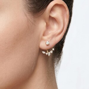 May include: A gold-toned ear jacket earring featuring a single round stud at the front and a curved, multi-stone drop piece that sits behind the earlobe, adorned with small, clear, marquise and round-cut stones arranged in a delicate, fan-like pattern.