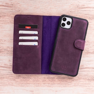 Peut inclure: Un étui de téléphone en cuir violet avec un design portefeuille. L'étui est ouvert, révélant des fentes pour cartes et un intérieur violet. Un téléphone est placé dans l'étui, sécurisé par une fermeture magnétique. L'étui est sur une surface en bois clair.