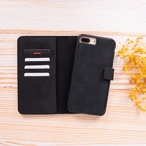 Peut inclure: Ensemble de portefeuille et d'étui de téléphone en cuir noir. Le portefeuille comporte des fentes pour cartes et un compartiment à billets. L'étui de téléphone a une fermeture magnétique. L'ensemble est présenté ouvert sur une surface en bois clair.