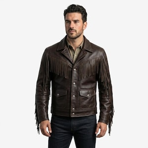 Könnte beinhalten: Braune Lederjacke mit Fransen an Brust, Schultern und Ärmeln. Die Jacke hat eine Knopfleiste, zwei Brusttaschen und einen Kragen. Das Model trägt ein grünes Hemd und dunkelblaue Jeans.