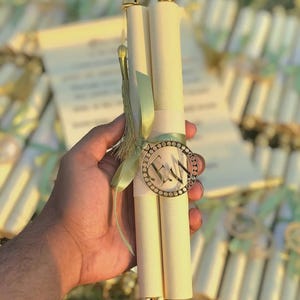 May include: Cream-coloured scroll invitations with gold accents. Each scroll is held together with a gold-rimmed medallion and a green ribbon. The scrolls have gold finials and a gold tassel.