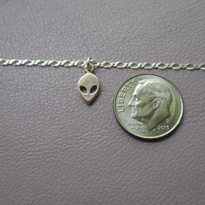 Puede incluir: Un collar de cadena de plata con un peque&ntilde;o dije de extraterrestre. El dije es del tama&ntilde;o de una moneda de diez centavos.