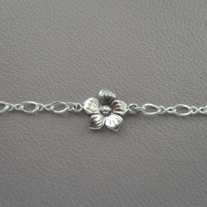 May include: A silver chain bracelet with a small silver flower charm.