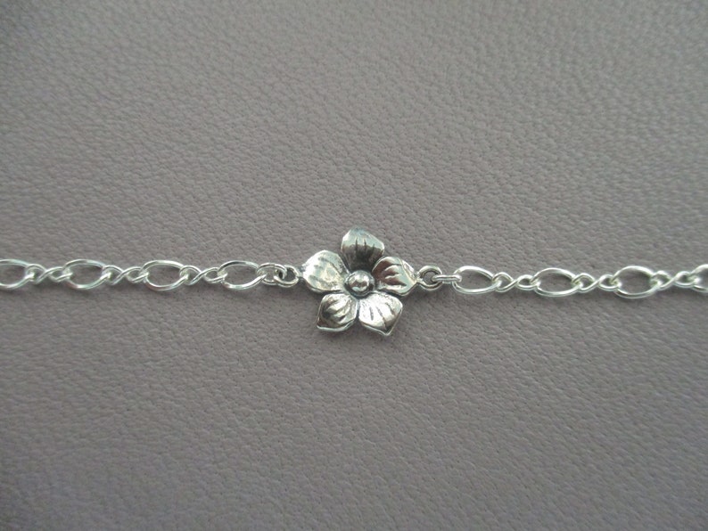 May include: A silver chain bracelet with a small silver flower charm.