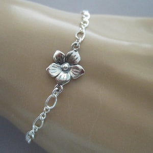May include: A silver chain bracelet with a delicate flower charm. The flower charm has a detailed design and is attached to the chain with a small loop.