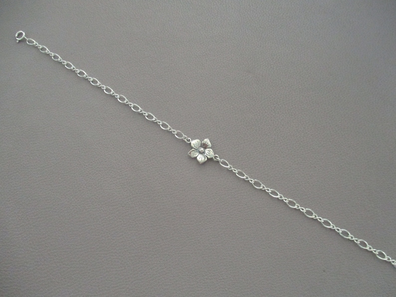 May include: A silver chain bracelet with a delicate flower charm.