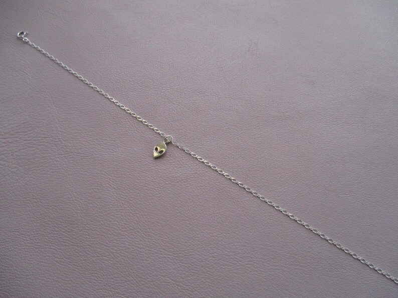 Puede incluir: Un collar de cadena de plata con un peque&ntilde;o dije de extraterrestre.