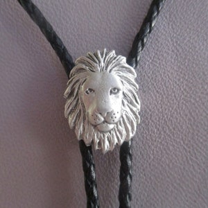 May include: A silver lion head bolo tie with black braided cords.