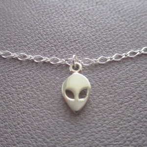 Puede incluir: Un collar de cadena de plata con un peque&ntilde;o colgante de cabeza de extraterrestre de plata.