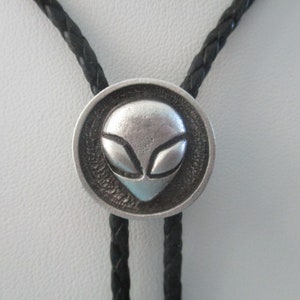 May include: A black braided bolo tie with a silver alien head pendant.