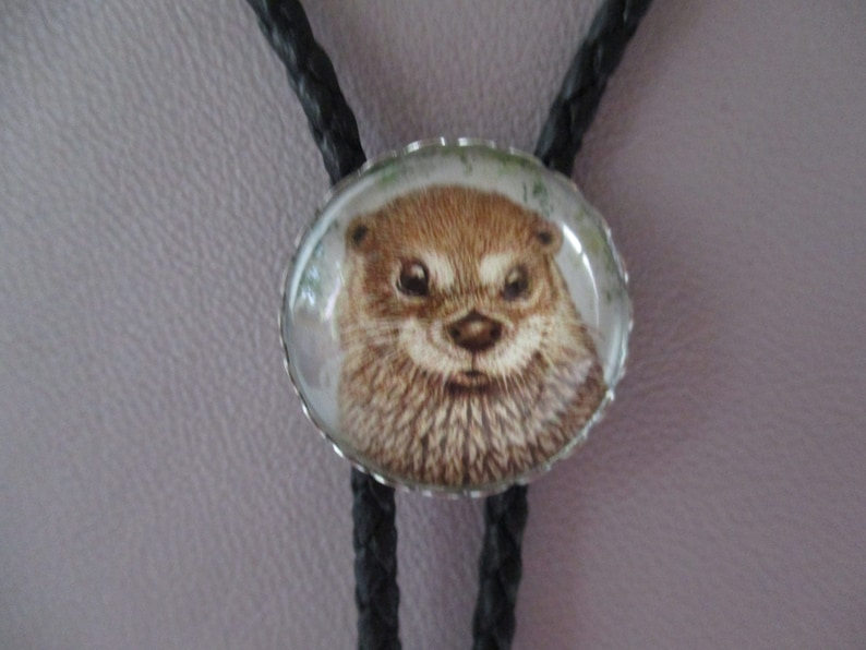 May include: A black bolo tie with a round silver-toned pendant featuring a close-up image of an otter's face.