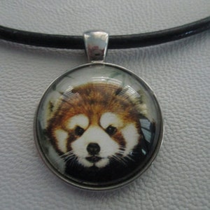 May include: A red panda face is featured on a round glass pendant, set in a silver frame. The pendant is attached to a black leather cord.