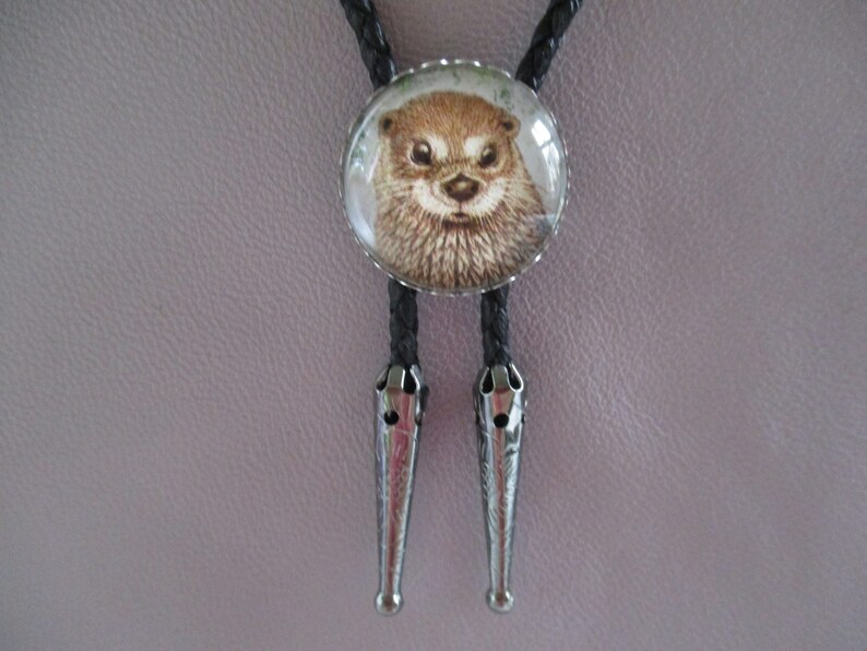 May include: A black bolo tie with a round glass pendant featuring a close-up image of an otter's face.