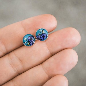 Peut inclure: Une paire de boucles d'oreilles clous en argent avec un fond bleu et un motif floral violet.
