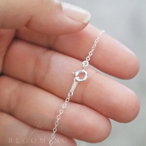 May include: A delicate silver chain necklace featuring a round spring ring clasp. The metal has a bright, reflective finish. A watermark with the text BLOOMING thread HANDMADE is visible in the lower left corner of the image.